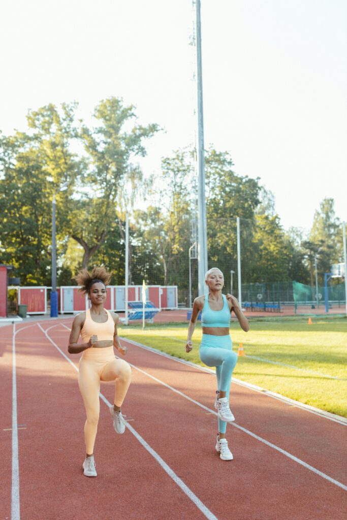 Two women jogging on an outdoor track under sunlight, promoting fitness and health.