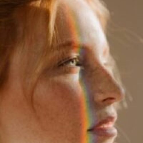 pexels-photo-4974360-4974360 Elegant portrait of a redhead woman with rainbow light across her face, highlighting freckles and beauty.